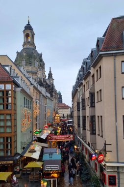 Dresden, Germany, December 8, 2024: Bustling christmas market street in a historic european city during the festive season. features illuminated decorations, lively crowds, and classic architecture with a prominent church dome in the background. clipart