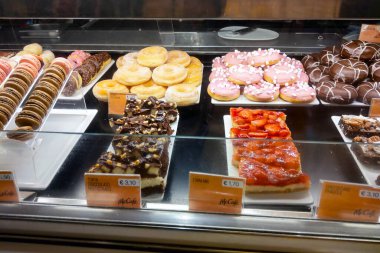 Milan, İtalya, 1 Aralık 2024: Donut, badem kurabiyesi, çikolata ikramı ve meyveli barlardan oluşan çeşitli hamur işleri ve tatlıların yer aldığı bir kafe tatlı gösterisi. Avro cinsinden gösterilen fiyatlar Avrupalı bir konuma işaret ederken, düzgünce düzenlenmiş fiyatlar 