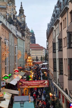 Dresden, Almanya, 8 Aralık 2024: Kostümlü, Almanya 'da hareketli bir Noel pazarı tarihi mimari altında şenlikli ışıklarla süslenmiş canlı tezgahlar sergiliyor. Kalabalık, kültürel cazibe ve kış ruhuyla dolu bir sahnede tatil alışverişinin keyfini çıkarıyor.