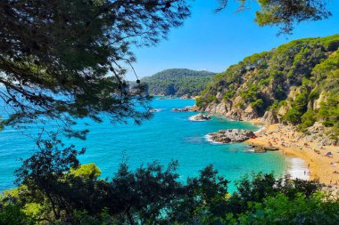 Bereketli bitki örtüsü, berrak turkuaz sular ve kayalık kayalıklarla çevrili gözlerden uzak bir sahile sahip çarpıcı bir kıyı manzarası. Güneşlenirler kumlu sahilde, sakin bir yaz kaçışının tadını çıkarırlar..