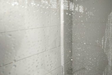 Parlak cam fayanslardaki şeffaf su damlacıkları modern bir duş ortamında rahatlatıcı bir atmosfer yaratıyor. Temizlik, rahatlama ve modern banyo tasarımı ile ilgili kavramlar için ideal..