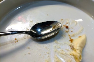 A close-up of a nearly empty dessert plate, showcasing a metal spoon with traces of creamy dessert and crumbs. the image conveys the satisfaction of a delicious gourmet meal, emphasizing a moment of indulgence and culinary enjoyment. clipart