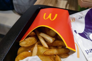 Barselona, İspanya, 26 Aralık 2024: Bir servis tepsisine yerleştirilmiş kırmızı bir kapta kızarmış patates kızartması, popüler bir fast-food yemek deneyimini gözler önüne seriyor. İştah açıcı atıştırmalığa mükemmel bir Q portresi çizen baharatlar eşlik eder.