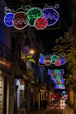 Barselona, İspanya, 25 Aralık 2024: Canlı sokak dekorasyonları renkli tatil temalı ışıkların yer aldığı bir şehir caddesini gece aydınlatıyor. Noel 'in neşeli atmosferi, canlı bir şehir yolunun üzerinde asılı duran parlak süslemelerle..