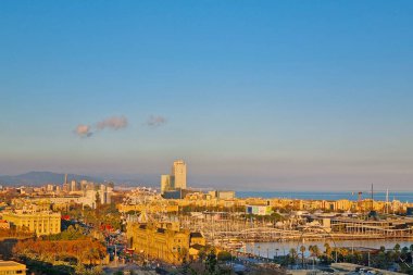 Barselona, İspanya, 1 Ocak 2025: Altından günbatımı gökyüzü altında hareketli bir limanın, seçkin bir dönme dolabın ve uzak dağların bulunduğu çarpıcı bir şehir manzarası. Şehir manzarası sakin bir rıhtımla tamamlanır., 