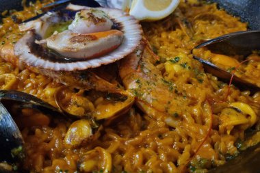 Canlı ve iştah açıcı bir deniz ürünleri paellası mükemmel pişirilmiş midye, dolgun midye ve karides içerir. Limon dilimi ile süslenmiş, yemek vitrinleri zengin, baharatlı altın pirinç, aşçılık için ideal bir sunumla tamamlanmış.