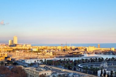Barcelona, İspanya, 1 Ocak 2025: Açık, mavi bir gökyüzü altında kentsel mimari ile çevrili, teknelerle dolu pitoresk bir limanın yer aldığı, altın saat boyunca hareketli bir Akdeniz liman şehrini görmek. Sakin denize ve aydınlatılmış binalara.