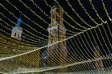 Zaragoza, İspanya, 26 Aralık 2024: Aydınlatılmış sicim ışıkları gece gökyüzüne karşı zarif, tarihi kuleler örterek şenlikli bir atmosfer yaratıyor. Tatil kutlamaları, şehir dekorasyonu ve şehir tasarımı için mükemmel..