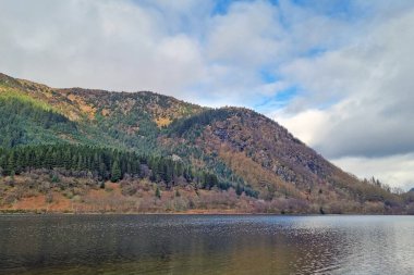Bereketli yeşil ormanlarla çevrili sakin bir göl ve parlak mavi gökyüzünün altındaki engebeli tepeler. Manzara huzur verici, doğal bir ortam sunuyor. Rahatlama ve doğa takdiri için ideal..