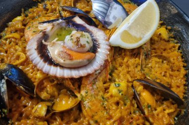 İçinde safran katılmış pirinç, karides, midye ve limon dilimli istiridye bulunan geleneksel İspanyol deniz ürünleri. canlı renkler ve zengin dokular mutfak sunumları ve gıda temalı projeler için idealdir.