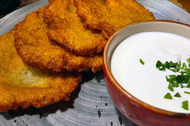 Bir kase kremalı ekşi kremanın yanında taze otlarla süslenmiş çıtır patatesli krep. Bu iştah açıcı yemek dokuların ve tatların mükemmel bir karışımını vurgular, yemek ve özel toplantılar için ideal.