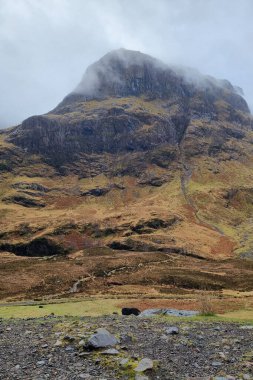 Sis kaplı zirvesi olan görkemli, heybetli bir dağ sakin bir manzaraya hükmediyor. Engebeli arazi ve toprak renkleri, el değmemiş vahşi doğanın doğal güzelliğini ve ihtişamını gösteren sakin bir atmosfer yaratıyor..