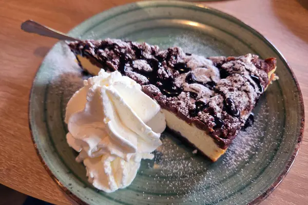 Çikolata soslu nefis bir dilim kremalı cheesecake, kırsal seramik tabakta bol miktarda krem şanti ile servis edilir, hoşgörü ve gurme tatlı estetiğini çağrıştırır..