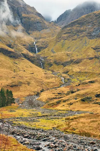 Çarpıcı dağ manzarasında engebeli yamaçlardan çağlayan şelaleler var. Kayalık akarsu, sisli zirvelerle çevrili, altın sonbahar manzarası boyunca esiyor. Huzuru ve doğal güzelliği çağrıştırıyor..