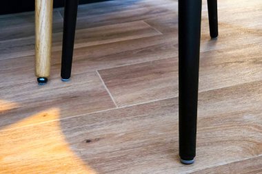 Sıcak tonlu ahşap zemine karşı dizayn edilmiş ahşap ve metal sandalye bacaklarının zıt dizaynını içeren modern minimalist iç mekan. Güneş ışığı ince gölgeler bırakır, zarif zarafet ve uzayın basit güzelliği..