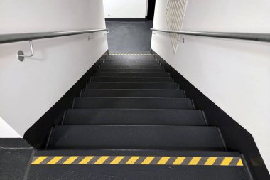 Metal tırabzanlar ve kendine özgü sarı güvenlik şeritleri olan gösterişli, minimalist bir tasarıma sahip endüstriyel merdiven. Nötr renk paleti ve temiz çizgiler çeşitli ticari ve endüstriyel alanlar için modern, işlevsel bir estetik sunar