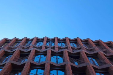 Geometrik desenler, berrak mavi gökyüzüne karşı çağdaş bir binanın çarpıcı ön cephesini oluşturur. Simetri ve keskin açılar modern mimari yenilik ve kentsel tasarım estetiğini vurgular.