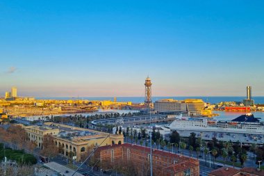 Barselona, İspanya, 1 Ocak 2025: Barselona liman bölgesinin günbatımında manzarası, şehir manzarası, Akdeniz manzarası ve ikonik mimari. Palmiye ağaçları, binalar ve dönme dolap, canlı bir şehir atmosferini yansıtıyor..