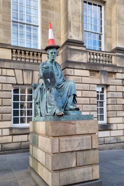 Edinburgh, İskoçya, 30 Mart 2025: Filozof David Hume 'un neşeli dokunuşlu bronz bir heykeli, klasik bir taş binanın önünde yer alan ve modern mizah ile tarihi önemi harmanlayan bir trafik konisi.