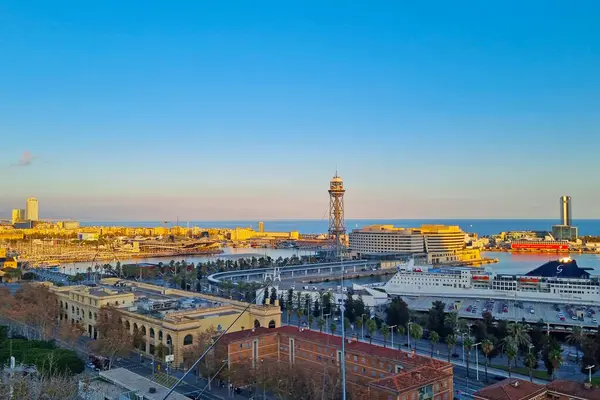 Barselona, İspanya, 1 Ocak 2025: Barselona liman bölgesinin günbatımında manzarası, şehir manzarası, Akdeniz manzarası ve ikonik mimari. Palmiye ağaçları, binalar ve dönme dolap, canlı bir şehir atmosferini yansıtıyor..