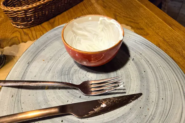 Bitmiş bir yemek takımında seramik tabağa konmuş çırpılmış krema kalıntılarıyla dolu boş bir seramik tatlı kasesi bulunur. Kullanılmış çatal ve bıçak. Tahta bir masada kasenin yanında dinleniyor. Bu da yakın zamanda tamamlanmış bir yemeği işaret ediyor..