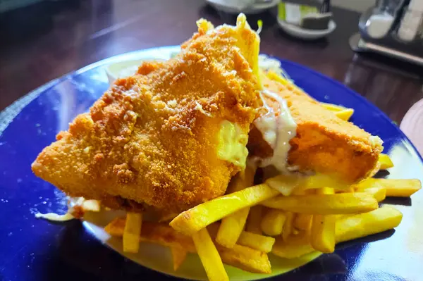 Kıtır kıtır, altın sarısı hırpalanmış balık canlı mavi bir tabakta cömert bir porsiyon patates kızartmasının üzerinde servis edilir. Zengin doku ve renk kontrastı bu mükemmel İngiliz konforlu gıdasını vurguluyor, doyurucu bir yemek için mükemmel..