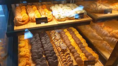 Fırın vitrininde çeşitli hamur işleri sergilenirken, kruvasan ve çikolata kaplı ikramlar da dahil olmak üzere cazip fırınlanmış gıdalar sunuldu. Tatlı ilhamı ve fırın tasarımı için ideal..