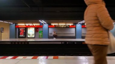 Barcelona, İspanya, 31 Aralık 2024: Santa Eulalia metro istasyonunda hareketli bir sahne peronda gezginler yer almaktadır. Bulanık bir figür yürüyüşü dinamizm katar, yalnız oturan bir yolcuyla çelişir. parlak işaret ve geometrik çizgiler
