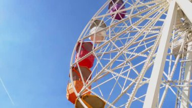 Parlak, renkli kamaraları olan dönme dolap parlak mavi gökyüzüne karşı kurulmuş. Perspektif karmaşık metal iskelet ve canlı renkler, eğlence, macera ve nostalji duyguları uyandırır..