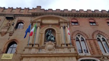 Bolonya, İtalya, 14 Mayıs 2024: İtalyan ve Avrupa bayraklarının bayraklarıyla çevrili, merkezi bir heykelin yer aldığı tarihi bir İtalyan binası cephesi. Yapı, karmaşık tuğla ve klasik mimari elementler sergiliyor