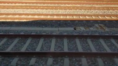 Çakıl taşlarında paralel metal rayları olan demiryolu rayları ışık ve gölge desenleri sergiliyor. Ulaşım, seyahat ve endüstriyel tasarım temaları için ideal.