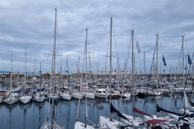 Barselona, İspanya, 3 Ocak 2025: Huzurlu ve bulutlu bir gökyüzü altında demirlemiş sayısız yelkenliyle dolu sakin bir marina. Deniz temalı tasarım, seyahat promosyonu veya kıyı yaşam tarzı betimlemesi için ideal, sükunet ve deniz kültürünün yakalanması.