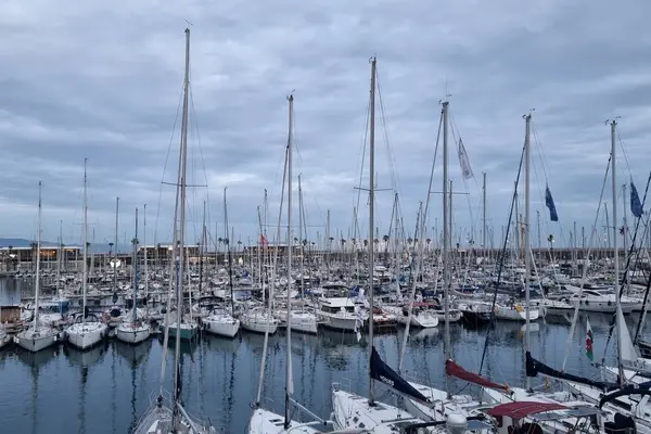 Barselona, İspanya, 3 Ocak 2025: Huzurlu ve bulutlu bir gökyüzü altında demirlemiş sayısız yelkenliyle dolu sakin bir marina. Deniz temalı tasarım, seyahat promosyonu veya kıyı yaşam tarzı betimlemesi için ideal, sükunet ve deniz kültürünün yakalanması.