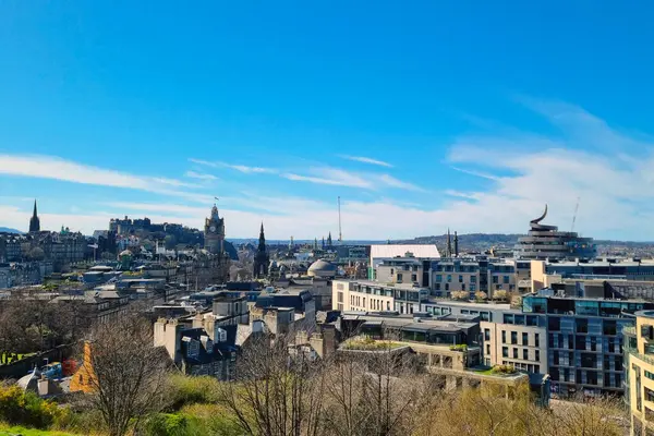 Edinburgh, İskoçya, 1 Nisan 2025: Edinburgh 'un canlı şehir manzarası parlak mavi gökyüzü altında tarihi ve modern mimarinin bir karışımını sergiliyor. Belirgin işaretler ve şehir yeşilliği olay yerine derinlik katarak şehrin cazibesini ve karakteristik özelliklerini yansıtıyor.
