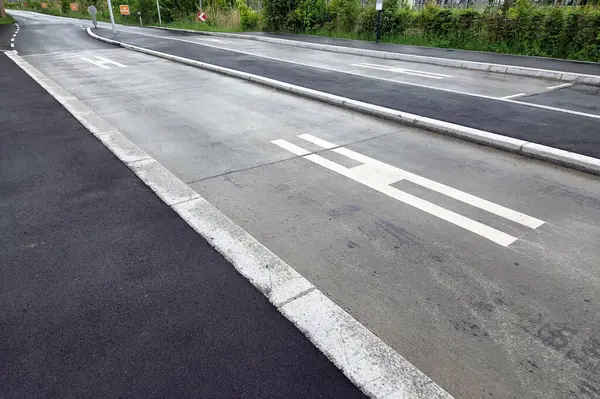 Belirlenmiş bir otobüs şeridi ve yaya sembolleri de dahil olmak üzere açık şeritli bir şehir yolunun geniş açılı görüntüsü. Sahne çevreleyen yeşillikler, verimli trafik yönetimi amaçlı kentsel planlama içeriyor.
