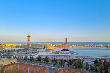 Barselona, İspanya, 1 Ocak 2025: Büyük bir yolcu gemisinin kıyıya yanaştığı canlı bir liman sahnesi. Batan güneş liman boyunca hafif bir parıltı saçarken palmiye ağaçları ve modern kuleler hareketli denizcilik atmosferini vurguluyor.