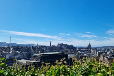 Edinburgh, İskoçya, 1 Nisan 2025: Edinburgh 'un şehir manzarası, canlı mavi gökyüzü altında tarihi mimarisini ve ikonik kalesini sergiliyor. Panoramik manzara, doğal manzara ve s ile çevrili antik ve modern yapıların karışımını vurgular.