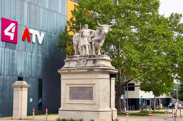 Viyana, Avusturya, 3 Mayıs 2025: Öküz ile çarpıcı bir veteriner heykeli, televizyon ağı logolarıyla süslenmiş modern bir binanın ön cephesinde belirgin bir şekilde duruyor. Sahne, tarihi sanatla çağdaş kemeri harmanlıyor.