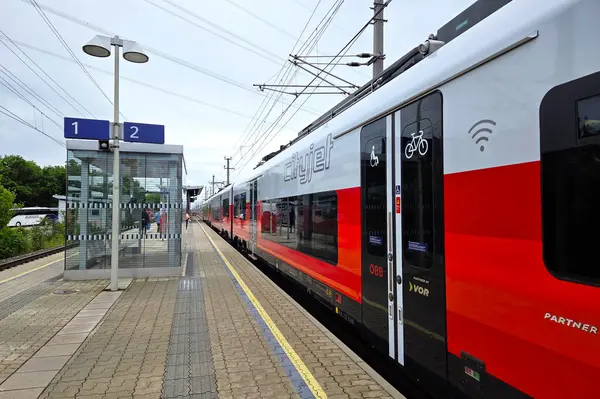Viyana, Avusturya, 4 Mayıs 2025: Çağdaş kentsel geçişi yansıtan kırmızı ve beyaz modern tren istasyonda bekliyor. Kablolar, tabela, bisiklet ve kablosuz ağ sembolleri toplu taşımacılıktaki kolaylık ve bağlantıyı vurguluyor.