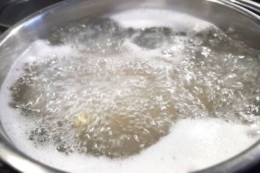 Suyun paslanmaz çelik bir tencerede güçlü bir şekilde kaynamasını, hızlı hareket ve kabarcıkları gösteren yakın çekim görüntüsü. Mutfak, mutfak ya da yemek pişirme temaları için mükemmel. Isı dönüşümü ve enerjiyi gösteriyor..