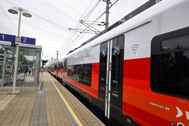 Viyana, Avusturya, 4 Mayıs 2025: Wi-fi ve bisiklet deposu gibi konforlara sahip bir Avrupa demiryolu platformunda lüks bir tren. Canlı kırmızı ve beyaz tasarım, çevre dostu iletişim için verimli bir seyahat sağlayarak modernliğini vurguluyor.