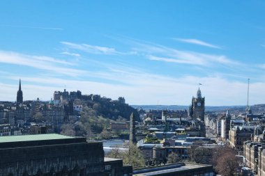 Edinburgh, İskoçya, 1 Nisan 2025: Edinburgh kalesinin bir tepede, tarihi mimaride ve açık mavi gökyüzünde görüldüğü panoramik manzara. Seyahat tasarımı için ideal, şehrin tarih ve modernite karışımını sergilemek.