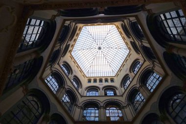 Viyana, Avusturya, 3 Mayıs 2025: Tarihi bir bina içerisindeki süslü, altıgen cam bir kubbenin altından bakın. Geometrik tasarım detaylı kemerler ve birden fazla pencere içerir, mimari zarafet ve simetri izlenimi yaratır..