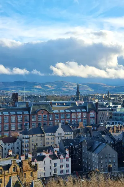 Edinburgh, İskoçya, 29 Mart 2025: Canlı şehir manzarası tarihi mimari barındıran yuvarlanan dağ zeminine karşı. Sahne, dinamik olarak bulutlu bir gökyüzü altında eski ve yeni yapıların karışımını vurguluyor, kentsel yaşamın özünü yakalıyor.