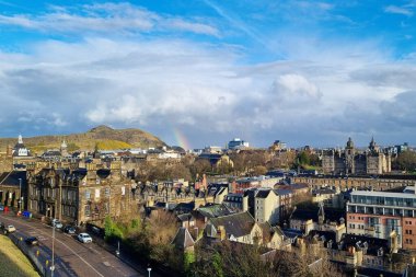 Edinburgh, İskoçya, 29 Mart 2025: Edinburgh 'un tarihi ufuk çizgisine bakan görüntü, gökyüzüne uzanan ikonik mimari bir zemin ve uzak bir tepe ile bir gökkuşağı yakalıyor. Doğal güzelliğin ve şehir manzarasının karışımı.