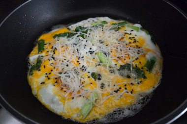 Taze kuşkonmaz ve erimiş peynirli lezzetli bir omlet, siyah susam tohumlarıyla süslenmiş, çubuksuz tavada pişiyor. Canlı renkler ve dokular onu besleyici bir kahvaltı ya da brunch için mükemmel kılar..
