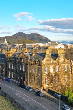 Edinburgh, İskoçya, 30 Mart 2025: Edinburgh, Arthur 'un koltuğunun pitoresk arka planına karşı tarihi mimarinin bir karışımını sergiliyor. Sahne parlak altın günbatımı renkleri, şehrin zengin kültürel mirası ve doğal güzelliği ile aydınlanıyor..