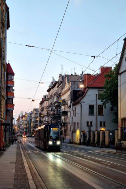 Wroclaw, Poland, May 30, 2025: A vibrant evening cityscape featuring a modern tram gliding along a historic street lined with charming buildings. the tranquil scene is set during dusk, with streetlights beginning to flicker against the pastel sky.