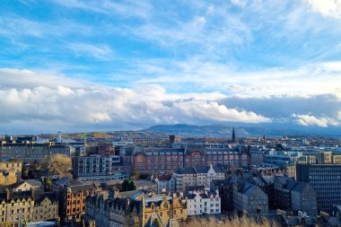 Edinburgh, İskoçya, 29 Mart 2025: Dinamik bir gökyüzü altında tarihi binaların ve modern yapıların yer aldığı canlı bir şehir manzarası. Mimarinin harmanlanması, geçmişi ve şimdiyi bir araya getirerek, kayan tepeler ve dramatik bir zemin oluşturur.