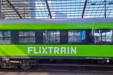 Berlin, Almanya, 26 Mayıs 2025: Çarpıcı bir yeşil film treni geniş cam bir çatı altında hareketli bir şehir istasyonunda duruyor, verimli ve çevre dostu bir yolculuk. Rengi endüstriyel arkaplan ve sürdürülebilir ulaşım ile çelişiyor..
